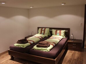 A double bed with two pillows and a blanket, a bedside table with a lamp, and a wooden floor. - Mier Gfallt's Appartement/Fewo, Bad, WC, 3 Schlafräume 5-Bettwohnung by Interhome (Saas-Fee)