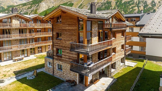 A multi-story wooden lodge with balconies, set against a mountainous backdrop. - Sonnegg Lodge 2.2 Appartement/Fewo Appartement/Fewo by Interhome (Saas-Fee)