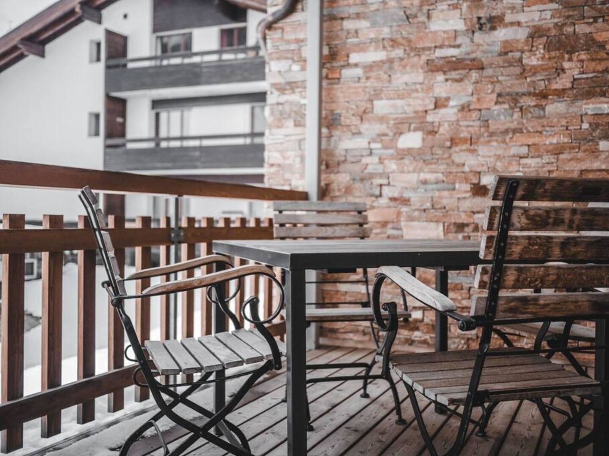 Une terrasse en bois avec une table et des chaises, un mur en briques et une rambarde.