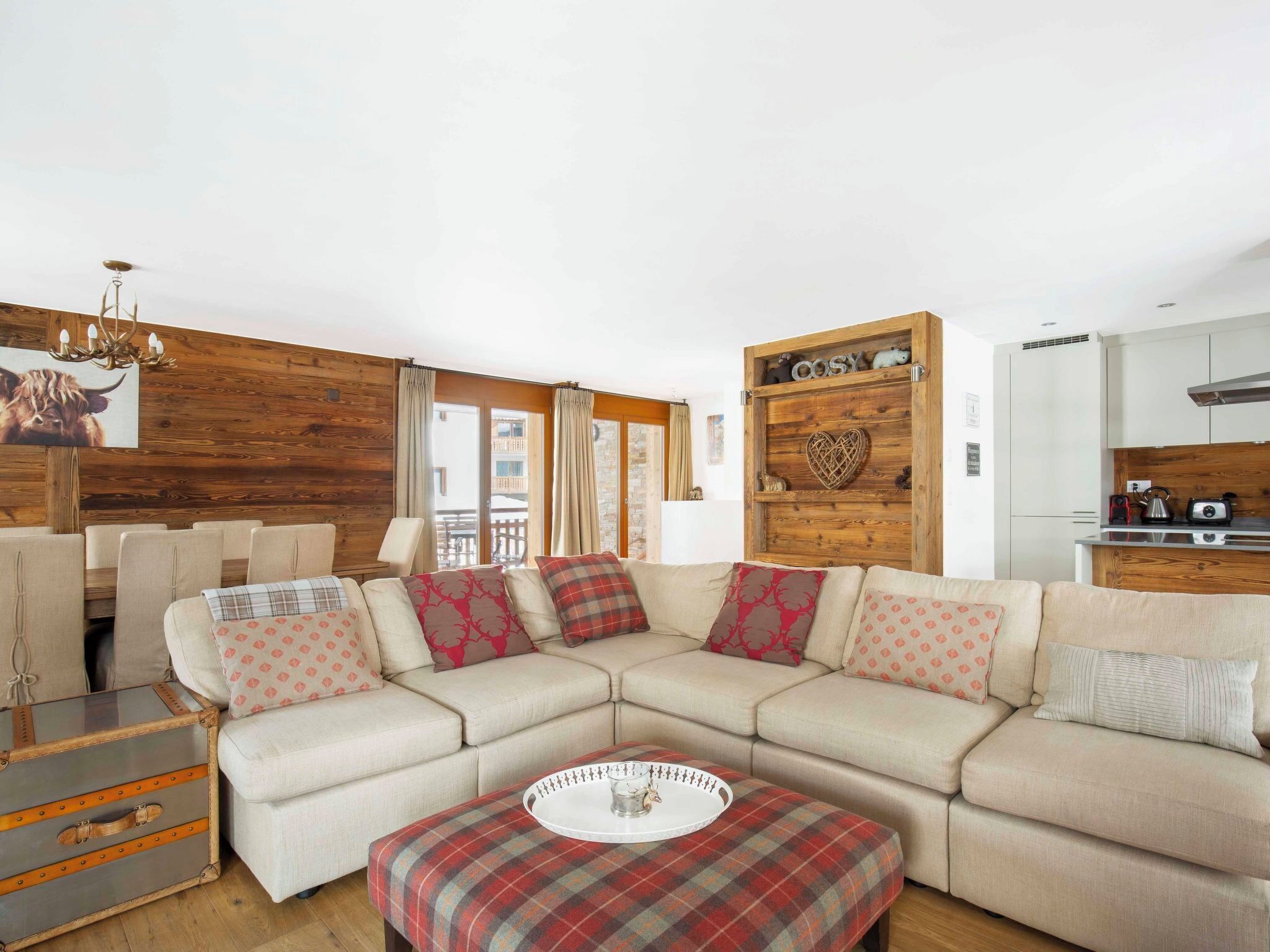 Una sala de estar acogedora con un sofá seccional, un reposapiés escocés, una pared de acento de madera y una zona de cocina.