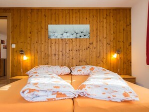 A double bed with floral bedding, two bedside lamps, and a wooden panel wall with a dandelion artwork. - Chalet Bambi Appartement/Fewo 6-Bettwohnung Nr. 1 by Interhome (Saas-Fee)