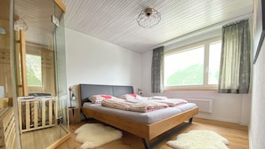 Een slaapkamer met een houten bed, een glazen douchecabine, een radiator en een raam met gordijnen.