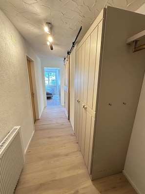 A hallway with a wooden floor, white walls, and a door with a radiator on the left. - Bettina Wellness Appartement/Fewo, Dusche oder Bad Bettina 3 by Interhome (Saas-Fee)