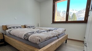 Makuuhuoneessa on puinen sänky, ikkunasta avautuu näkymä vuorille ja huoneessa on valkoinen vaatekaappi.