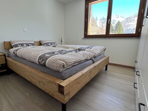 Ein Schlafzimmer mit einem Holzbett, einem Fenster mit Bergblick und einem weißen Kleiderschrank.