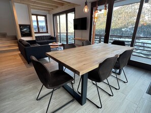 Ein zeitgemäßer Essbereich mit Holztisch und schwarzen Stühlen, einer Couch und einem Fernseher in einem Zimmer mit großen Fenstern.