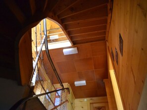Un intérieur en bois avec un escalier menant à un niveau supérieur, une fenêtre laissant entrer la lumière naturelle et une porte en bas.