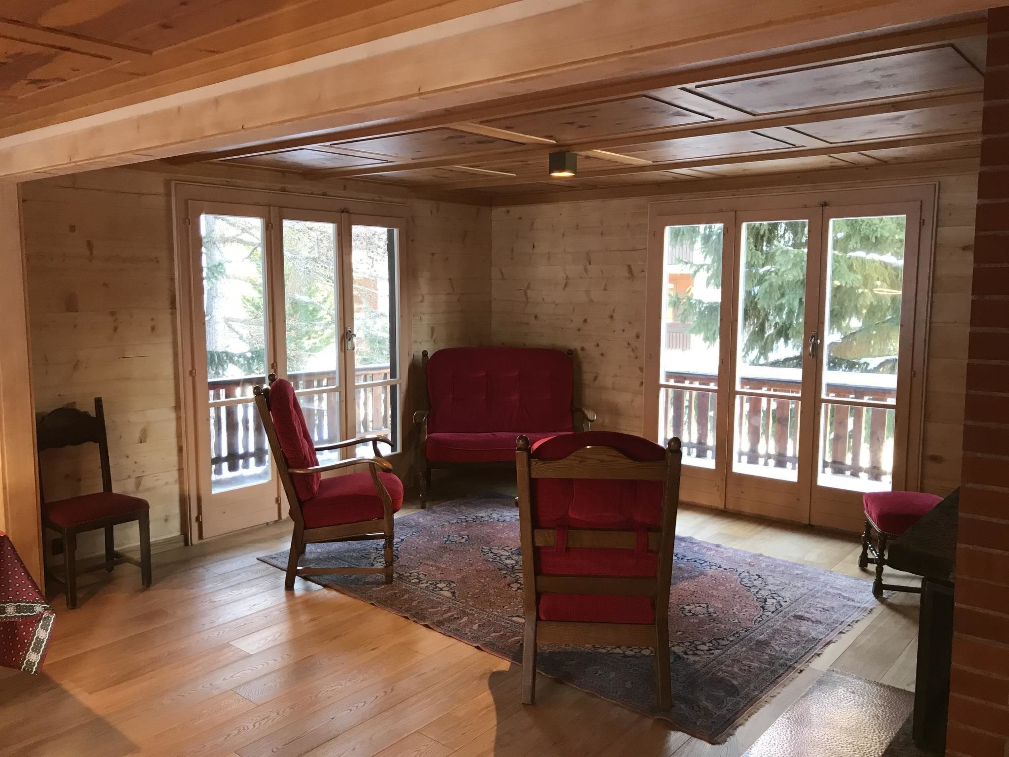Une pièce aux murs et au plafond en bois, dotée de grandes fenêtres, d’un canapé rouge et de deux fauteuils à bascule.