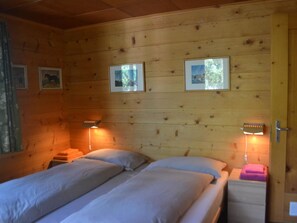 A wooden cabin room with two beds, a nightstand, and framed pictures on the wall. - Minga Mal Appartement/Fewo 8-Bettwohnung by Interhome (Saas-Fee)
