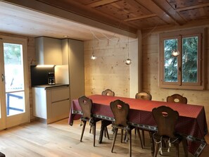 Ein Holzinterieur mit einem Esstisch für sechs Personen, Holzstühlen, einer Kaffeemaschine und Pendelleuchten.