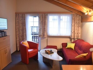 Ein möbliertes Wohnzimmer mit einem roten Sofa, einem roten Sessel, einem Couchtisch und einem Fernseher auf einem Schrank.