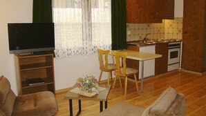 Un espacio habitable compacto con televisor, una mesa de comedor, dos sillas, un pequeño sofá y una kitchenette.