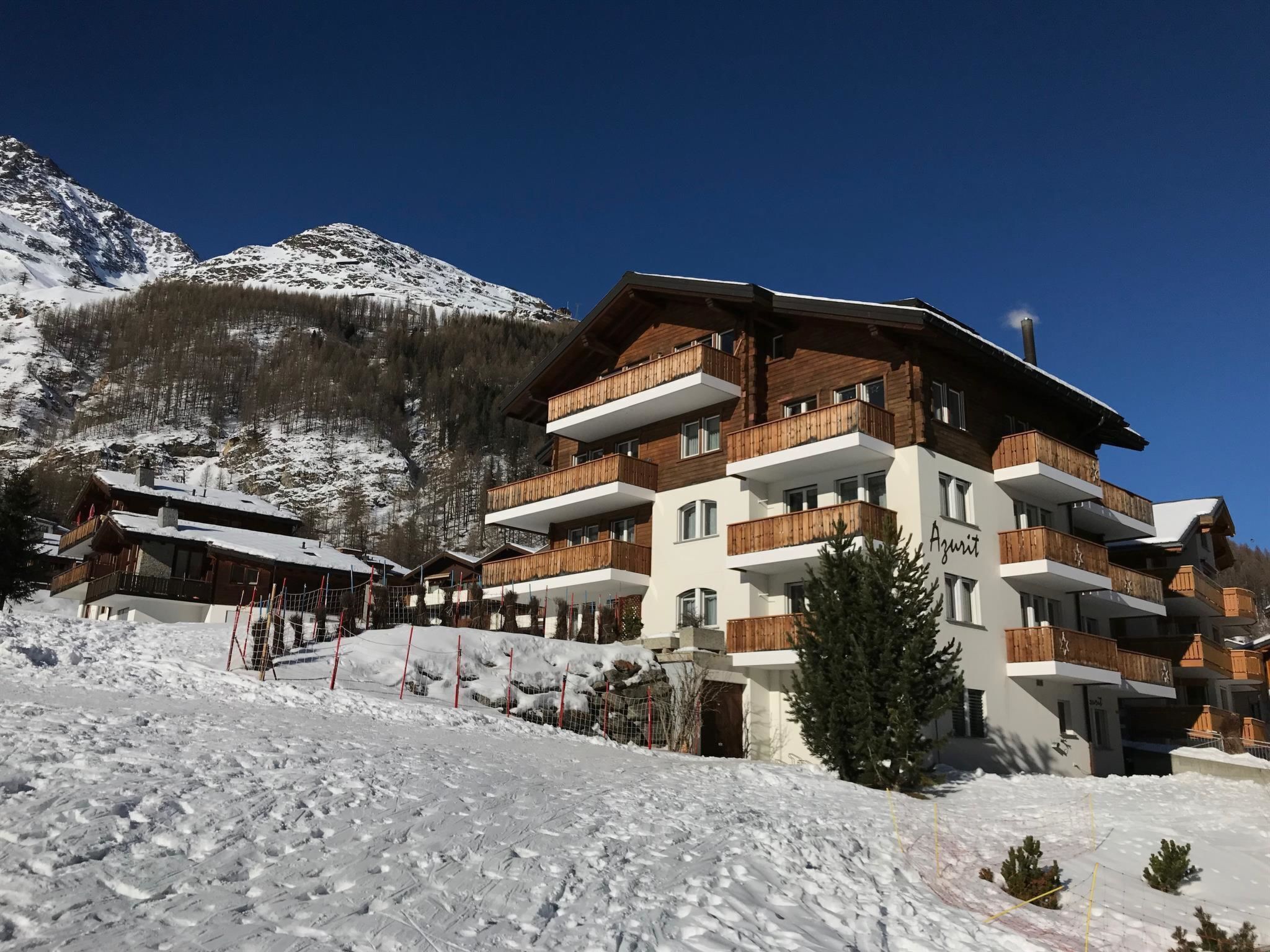 Ein mehrstöckiges Hotel mit hölzernen Balkonen vor einer verschneiten Bergkulisse.