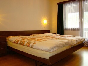 Een hotelkamer met een enkel bed, een nachtkastje, een wandlamp en een raam met gordijnen.