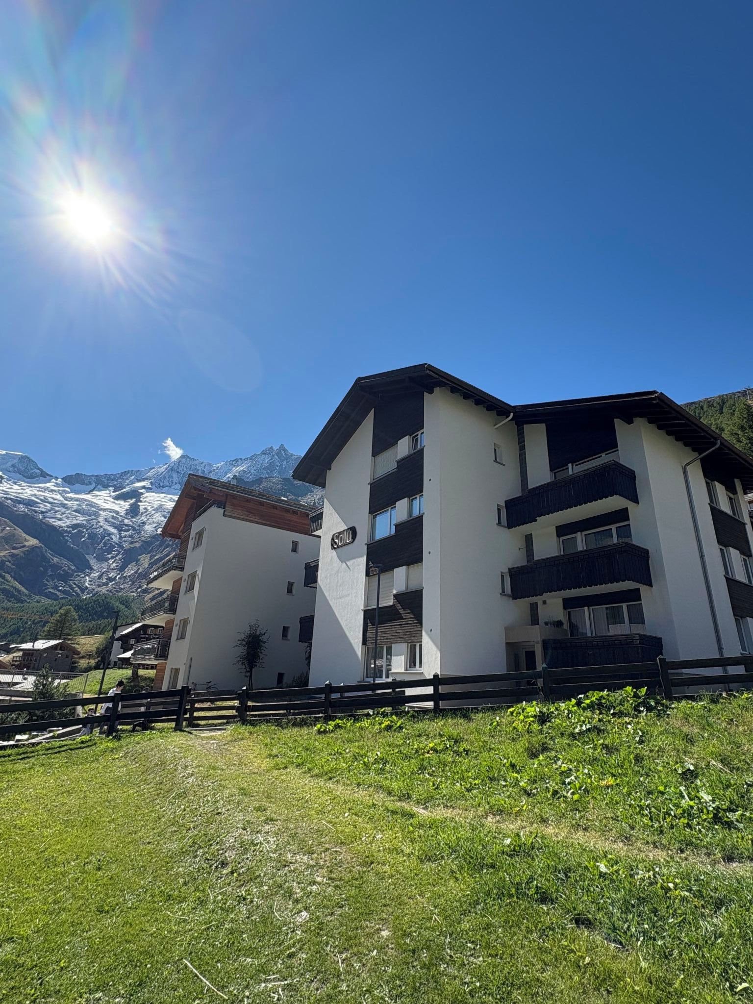 A multi-story building with balconies, set against a backdrop of snow-capped mountains.