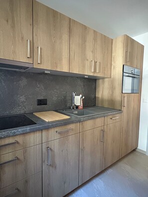 A modern kitchen with wooden cabinets, a black countertop, a stainless steel sink, and a glass oven door. - Haus Salü 5 Appartement/Fewo Appartement/Fewo by Interhome (Saas-Fee)