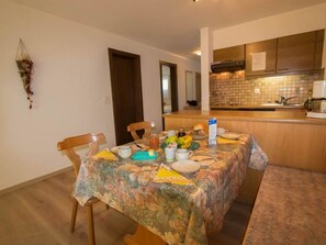 Een eetruimte met een tafel gedekt voor twee personen, een keuken met betegelde spatwand, en een hangplant.