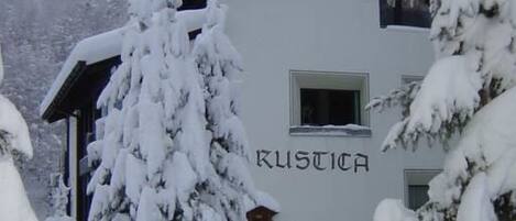 Ein Gebäude mit der Aufschrift 'KUSTICA' auf der Fassade, umgeben von schneebedeckten Bäumen.