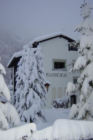 Ein Gebäude mit der Aufschrift 'KUSTICA' auf der Fassade, umgeben von schneebedeckten Bäumen.