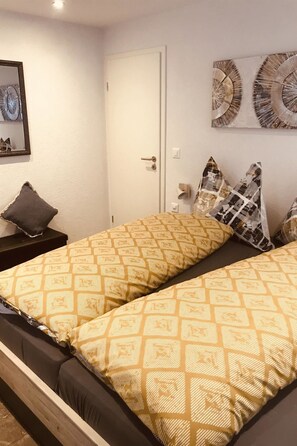 A bedroom with two beds, a nightstand, a door, and wall decorations. - Art Oase Appartement/Fewo 2-Bettwohnung by Interhome (Saas-Grund)