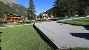 A mountainous area with a building that has multiple balconies and a grassy foreground. - Haus Vispa Appartement/Fewo Wohnung D by Interhome (Saas-Grund)