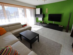 Ein modernes Wohnzimmer mit Sofa, Couchtisch und einem Flachbildfernseher vor einer grünen Wand.