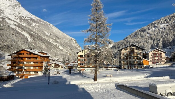 A snow-covered mountain resort with wooden buildings, a central tree, and a clear sky. - Haus Vispa Appartement/Fewo Wohnung D by Interhome (Saas-Grund)