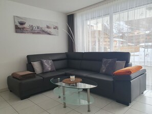 Una sala moderna con un sofá gris oscuro, dos cojines decorativos, una mesa de centro de vidrio y un letrero en la pared que dice 'HOME'.