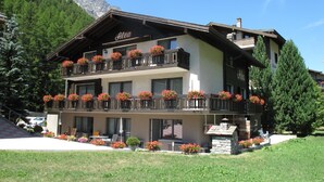 Un hotel de varios pisos con balcones decorados con jardineras, fachada de piedra y vistas a montañas.