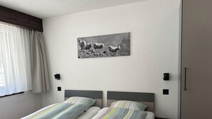 Habitación de hotel con dos camas, una ventana con cortinas, un cuadro colgado en la pared y dos apliques.