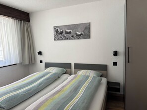 Habitación de hotel con dos camas, una ventana con cortinas, un cuadro colgado en la pared y dos apliques.