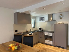 Una cocina moderna con horno integrado, pileta y estufa. Hay una mesa de comedor con frutas y una planta en la encimera.