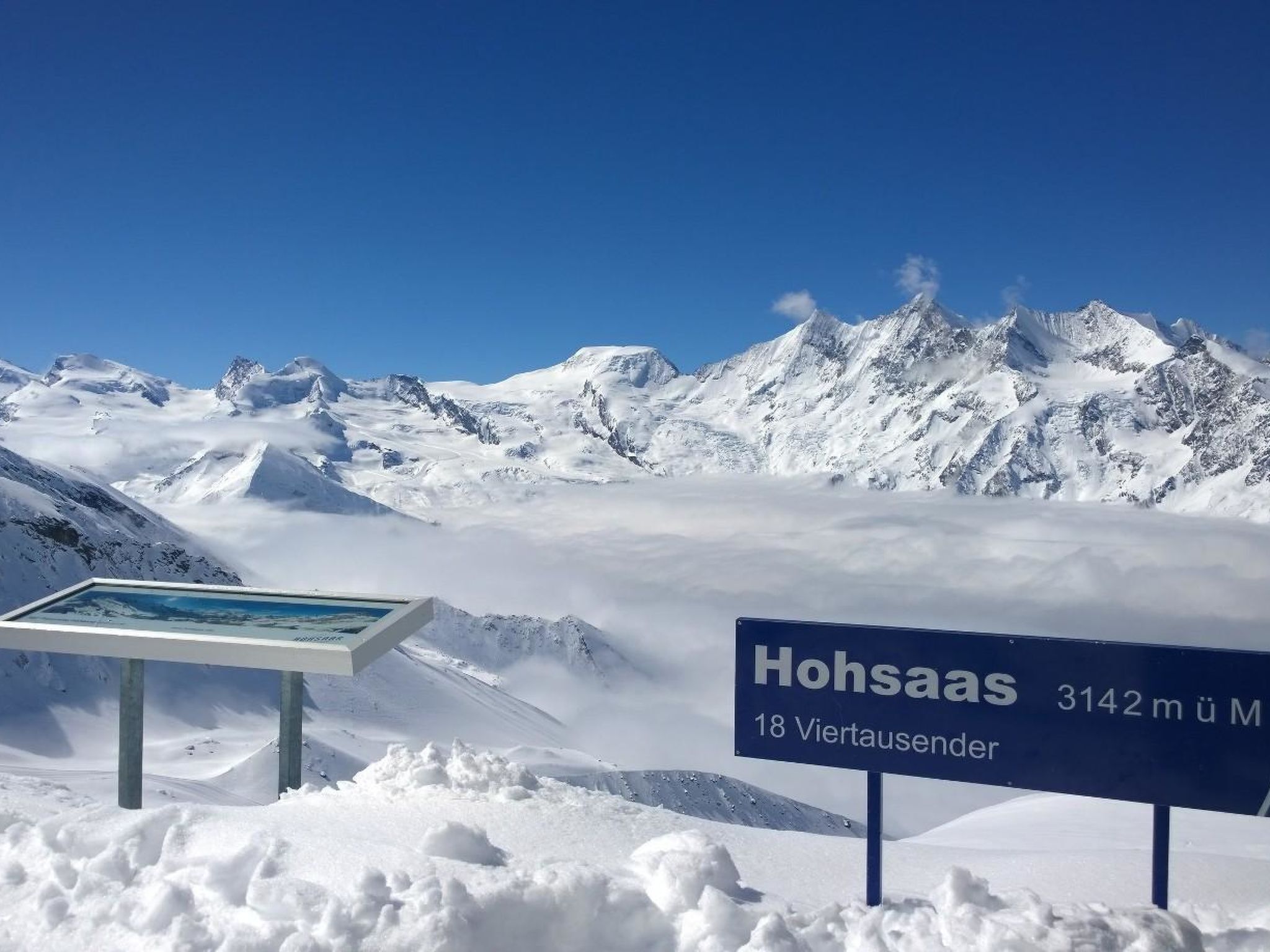 Un paysage de montagne enneigé, avec un panneau indiquant le nom « Hohsaas » et son altitude de 3142 mètres.
