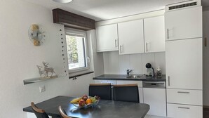 Una cocina moderna con armarios blancos, encimera negra y un comedor con una mesa dispuesta para dos.