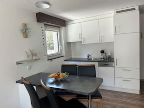 Una cocina moderna con armarios blancos, encimera negra y un comedor con una mesa dispuesta para dos.