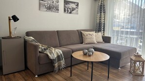 Una sala de estar moderna con un sofá, una mesa de centro y una lámpara. Hay dos cuadros enmarcados en la pared.