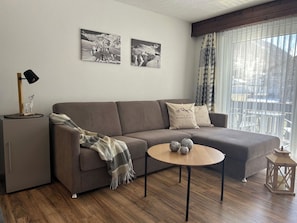 Una sala de estar moderna con un sofá, una mesa de centro y una lámpara. Hay dos cuadros enmarcados en la pared.