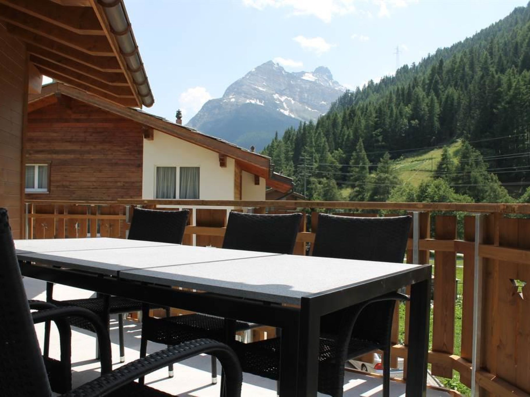 A wooden deck with a table and chairs, overlooking a mountain range.