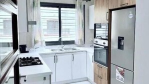 A compact kitchen with white cabinets, a stainless steel refrigerator, and a window with curtains. - Spacious Two-Bedroom Apartment with a Private Balcony and Terrace (Dakar)