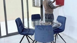 A person standing by a glass table with blue chairs, a red and white framed picture on the wall, and a sliding glass door in the background. - Spacious Two-Bedroom Apartment with a Private Balcony and Terrace (Dakar)