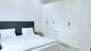 A bedroom with a large bed, white wardrobe, and a nightstand. - Spacious Two-Bedroom Apartment with a Private Balcony and Terrace (Dakar)