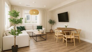 Una sala de estar con sofá, mesa de centro, mesa de comedor con sillas, televisor y dos plantas en macetas.
