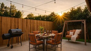 Un patio al aire libre con cerca de madera, una hamaca, una parrilla y una mesa lista para comer.