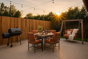 Eine Terrasse im Freien mit Holzzaun, einer Schaukel, einem Grill und einem Esstisch.