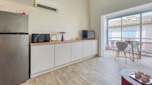 Een moderne keuken met een roestvrijstalen koelkast, een magnetron en een flatscreen televisie op een wit aanrecht. Er is een eethoek met een tafel en stoelen, en een groot raam met uitzicht op buiten.