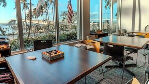 A conference room with a large window overlooking a beach, an American flag, and a table with a box of donuts. - 24th Floor City View. Luxury Downtown Apartment, Pool, Spa, Gym, Free Parking. (Fort Myers)