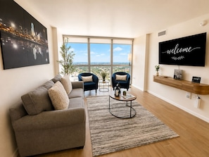 Una sala moderna con un sofá, dos sillones, una mesa de centro y un ventanal con vistas a la ciudad.