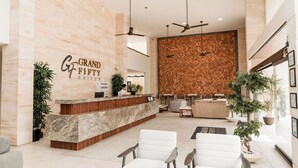 Un'area reception di un hotel con un bancone in marmo, posti a sedere bianchi, ventilatori a soffitto e una parete in legno.