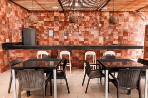 Restaurante com balcão de recepção, cadeiras de vime e parede revestida de azulejos.