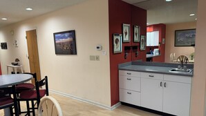 A modern kitchen with a dining area, wooden flooring, and a red accent wall. - Ground Level Condo 3 Community Pools and Tennis (Rehoboth Beach)
